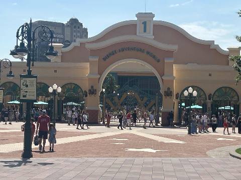 The entrance gate of an amusement park with a paved plaza and visitors.