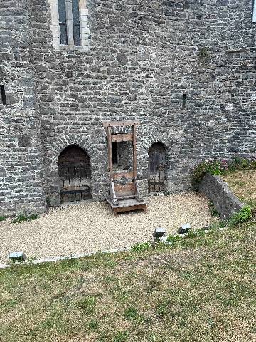 a wooden guillotine placed against a stone castle wall