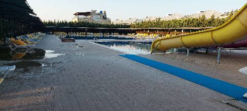 A swimming pool area at a resort with lounge chairs and a yellow water slide.