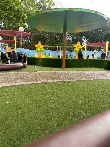 A playground with umbrella-shaped sun shades and people in a park setting.