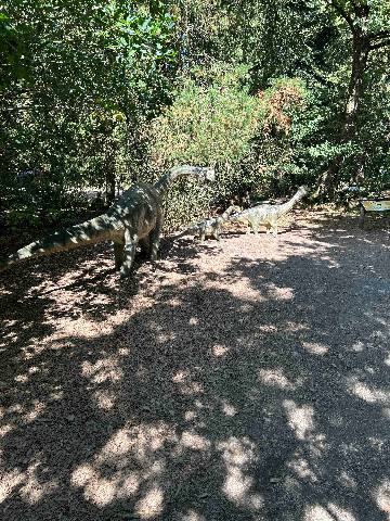 three dinosaur sculptures on a woodland path