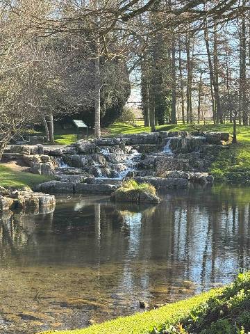 a tiered stone water feature in a garden park with a pond