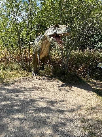 a dinosaur model in a park or forest setting
