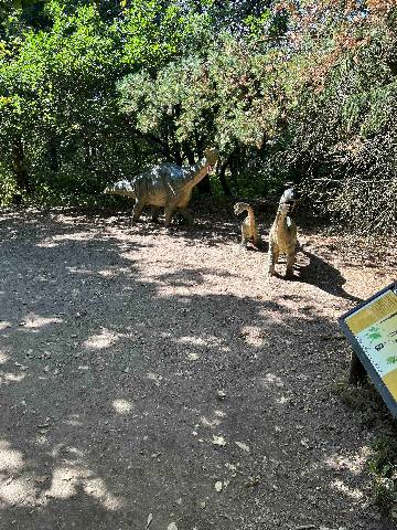 three dinosaur models on a dirt path in a park