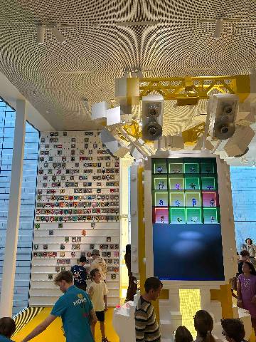 a brightly lit interior with a yellow overhead construction and digital display panels in a museum or interactive space