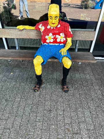 a sculpture made of plastic toy bricks on a bench outdoors