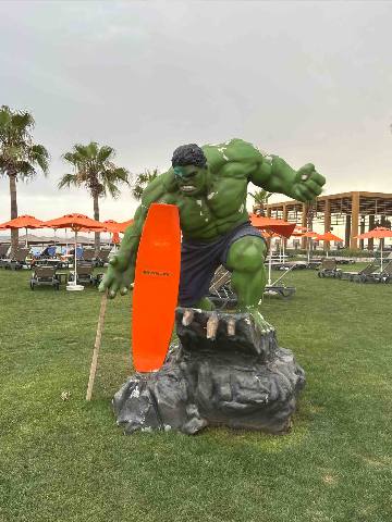 Antalya, Belek, a statue of a green character holding a surfboard on a grassy resort lawn