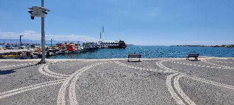 Edremit, Burhaniye, a harbor scene with docked boats and benches on a paved waterfront